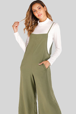 Sage culotte overalls with slender straps and side pockets, worn over a white turtleneck.