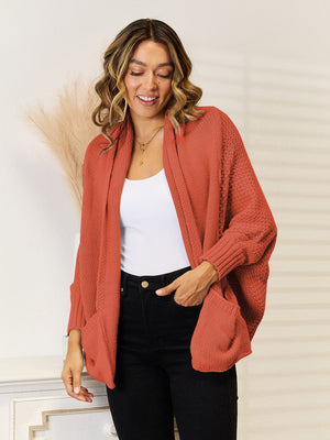 Rust acrylic knit cardigan with pockets and relaxed sleeves, styled with a white tank and black jeans.