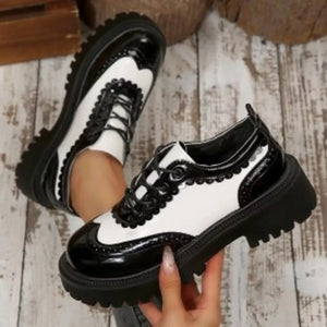 Round toe platform loafers with brogue detailing in black and white patent leather.