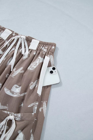 Brown cotton joggers with white western print, drawstring waist, and side pocket holding a phone.