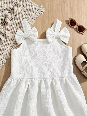 White baby dress with textured fabric, bowknot straps, and ruffled hem.