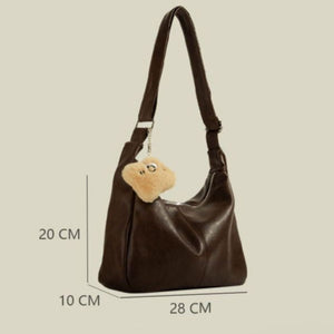 Brown pu leather crescent shoulder bag with fuzzy charm and adjustable strap.