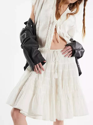 White tiered drawstring mini skirt with tassel detail and textured fabric.