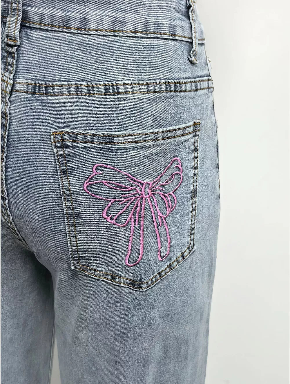Light wash denim jeans with pink embroidered bow detail on back pocket.