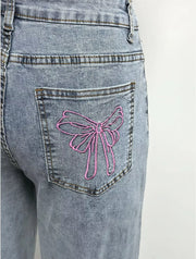 Light wash denim jeans with pink embroidered bow detail on back pocket.