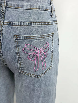 Light wash denim jeans with pink embroidered bow detail on back pocket.