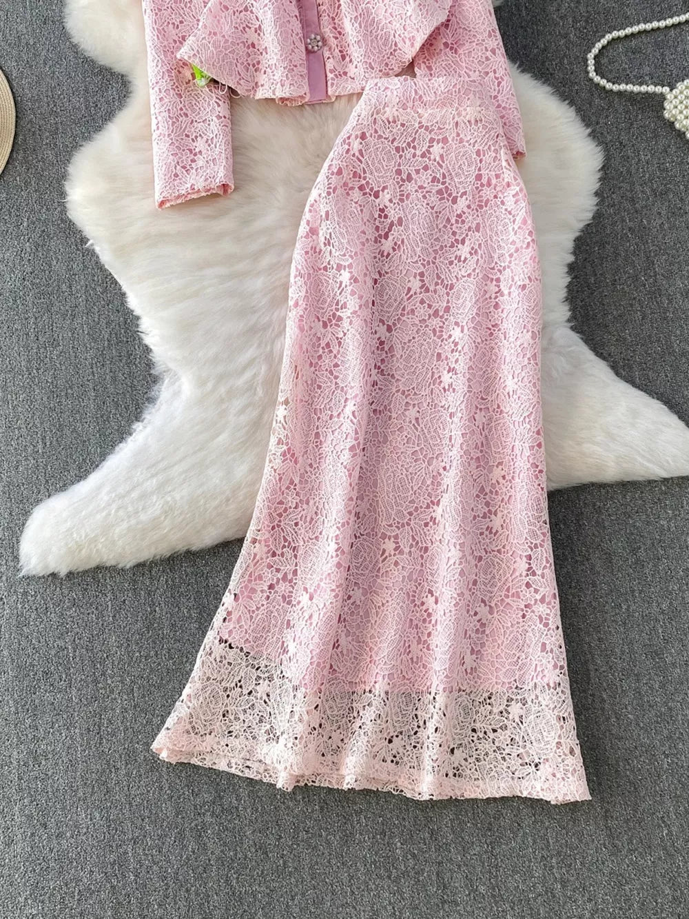 Blush pink lace two-piece ensemble with peplum top and long sleeves, and a matching lace skirt.