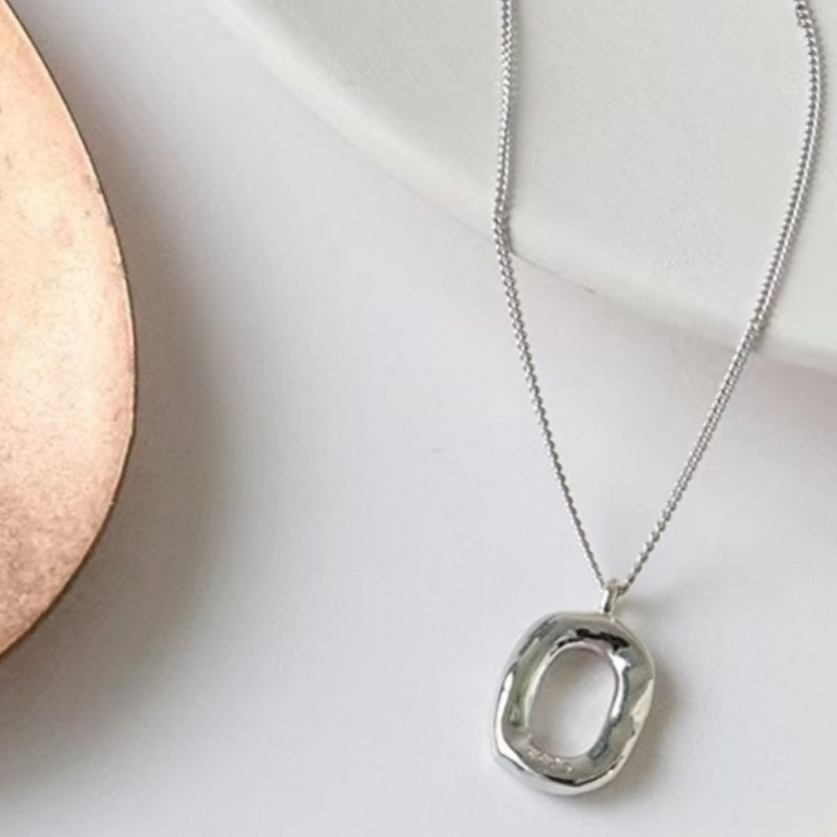 Silver geometric pendant necklace with a textured, organic shape on a delicate chain.