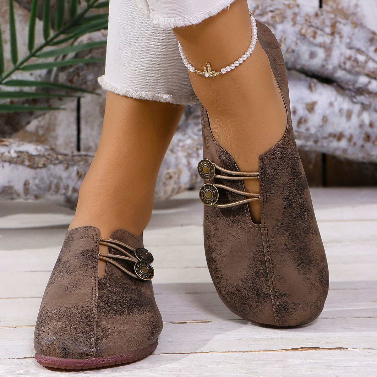 Dark brown round-toe casual flats with elastic straps and decorative buttons.