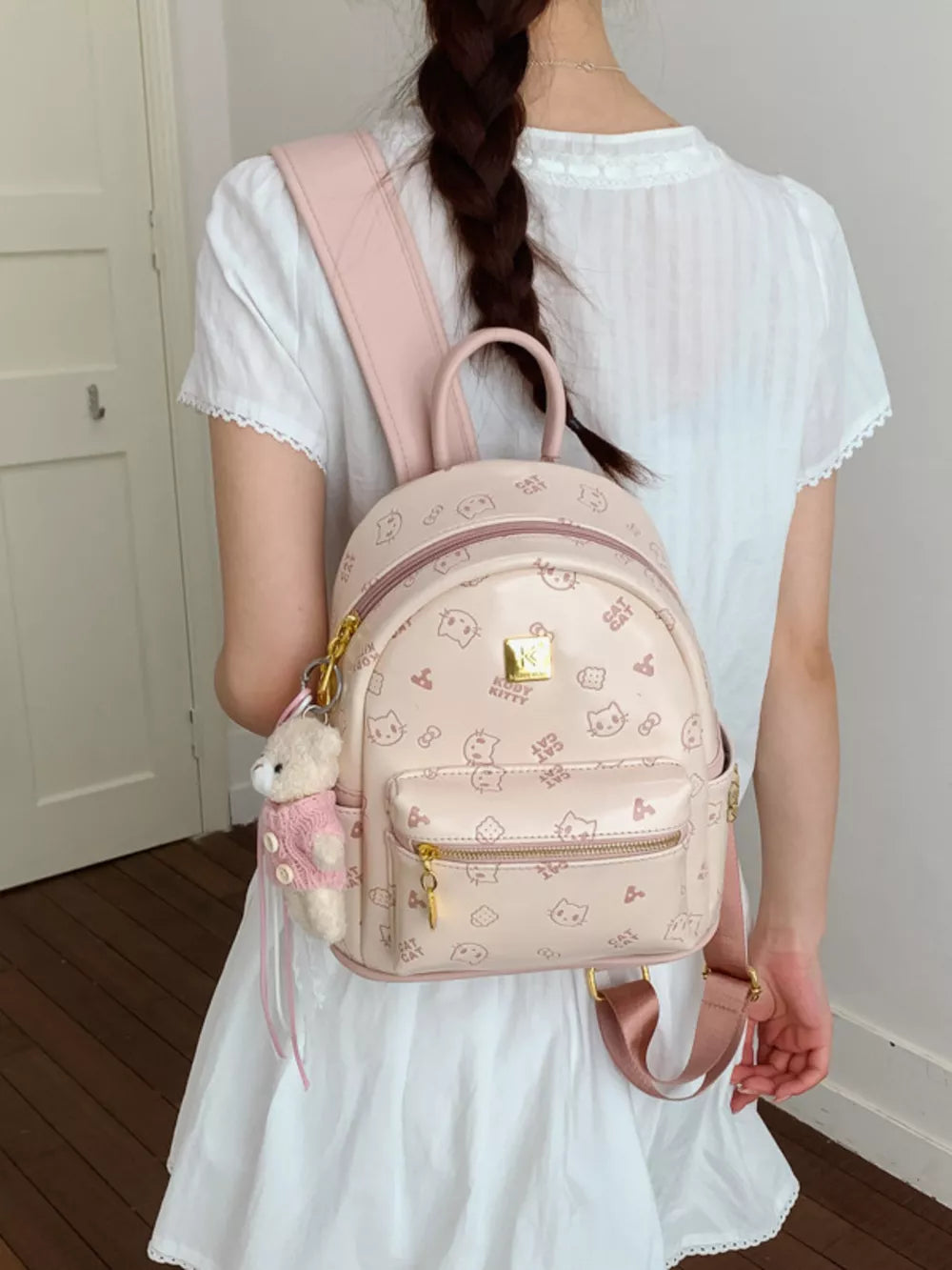 Blush pink mini backpack with allover cat print and bear charm, featuring a zippered front pocket.