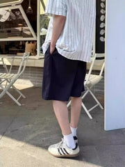 Navy blue relaxed fit chino shorts with pockets, styled with a striped shirt and sneakers.