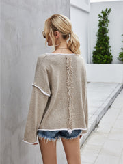 Beige knit pullover sweater with off-shoulder neckline, white trim, and fringe detail down the back.