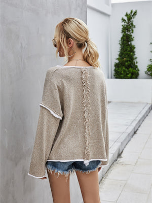 Beige knit pullover sweater with off-shoulder neckline, white trim, and fringe detail down the back.