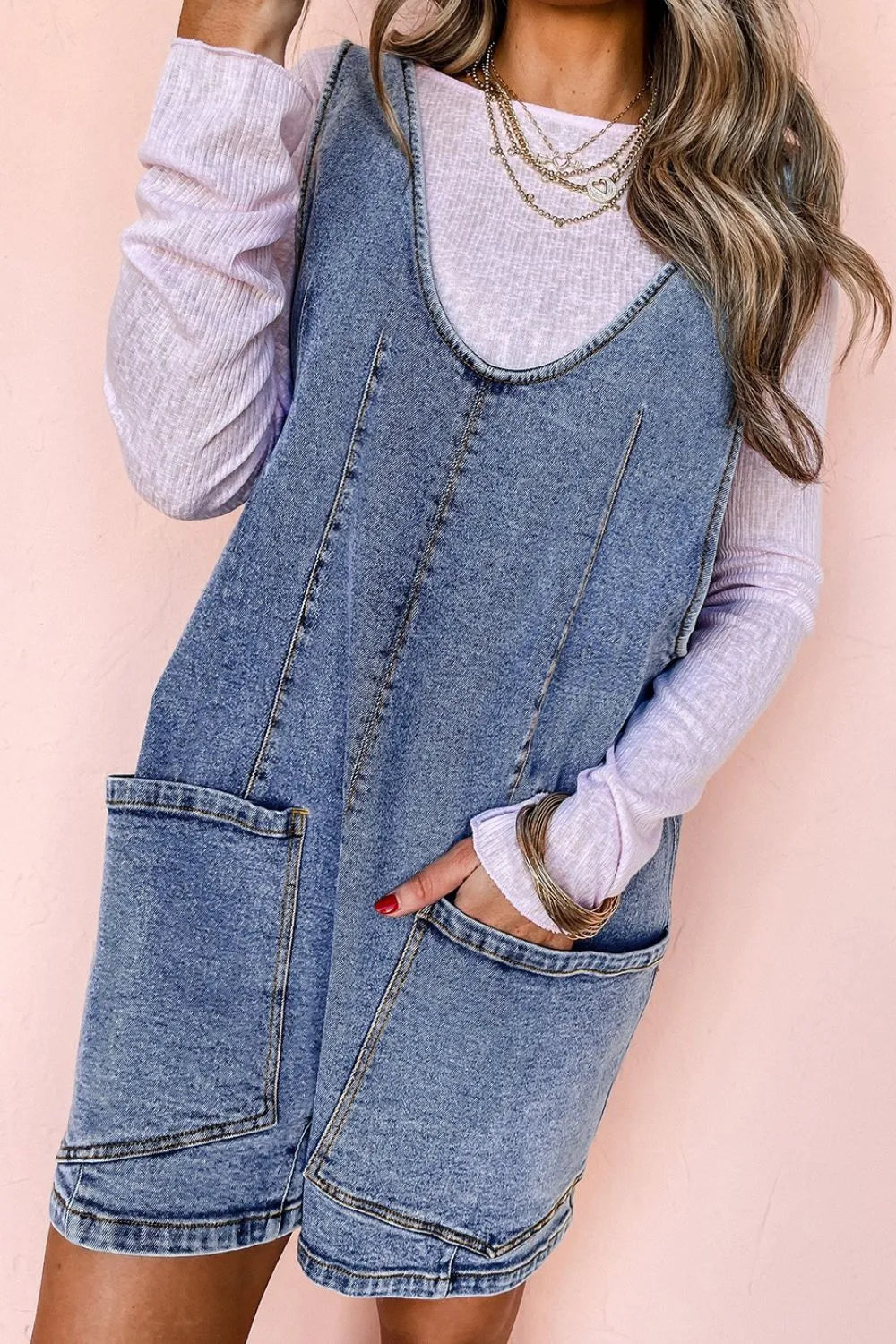 Acid wash denim romper with patch pockets and a v-neck, layered over a light purple long sleeve top.