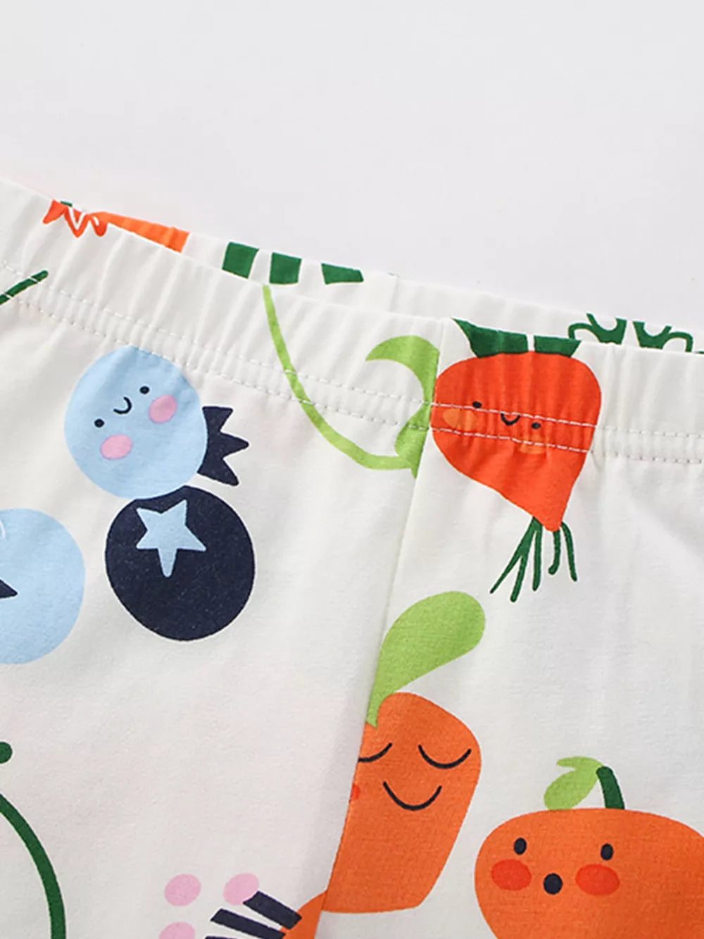 Baby outfit with playful cartoon fruit and vegetable print on white fabric.