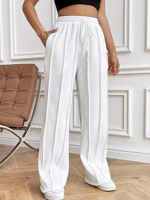 White pleated wide-leg lounge trousers with drawstring waist and pockets.