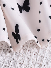 Baby dress with white fabric, black butterfly and polka dot print, and lace trim detail.