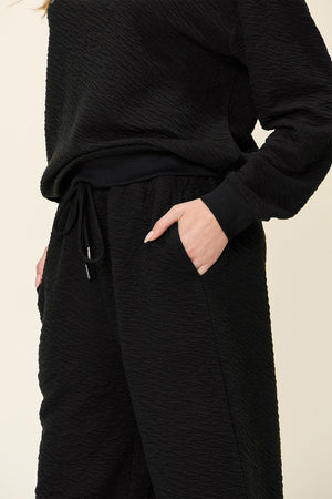 Black textured loungewear set with drawstring wide-leg pants and crewneck sweatshirt.