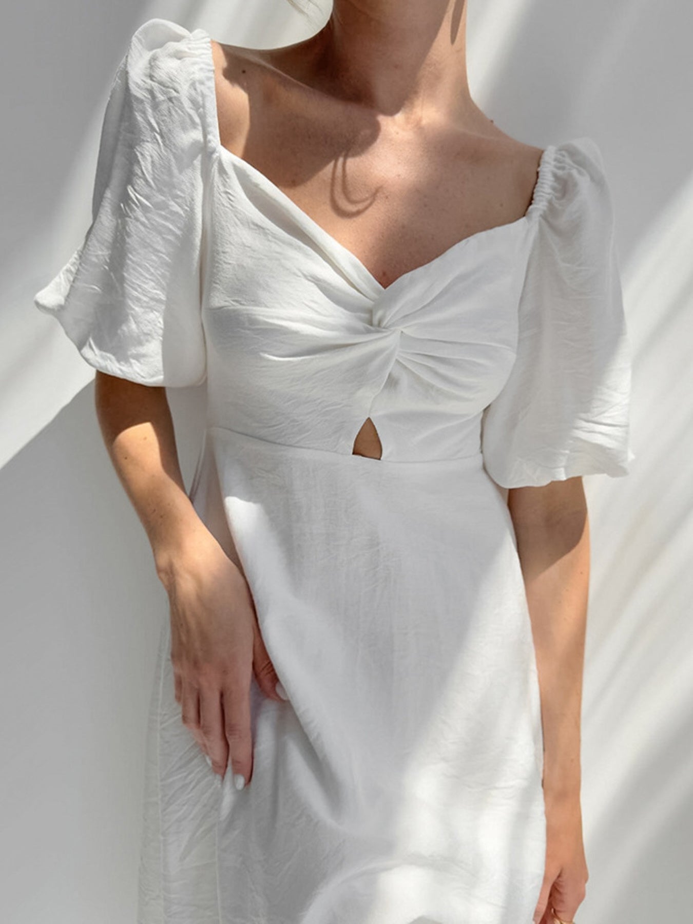 White midi dress with off-shoulder neckline, twisted front, cutout detail, and puff sleeves.