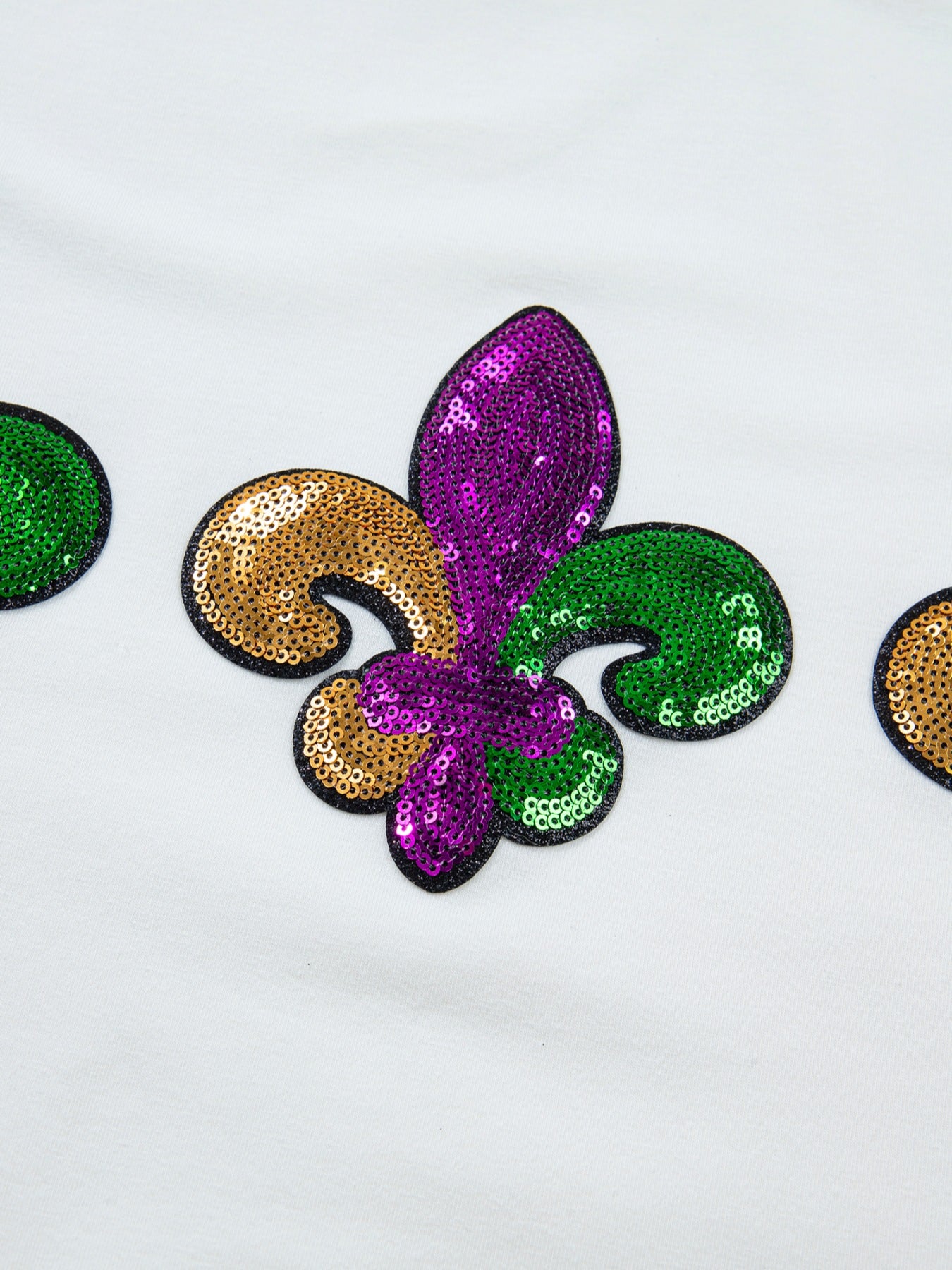 White cotton t-shirt with Mardi Gras fleur de lis sequin embellishments in purple, gold, and green.