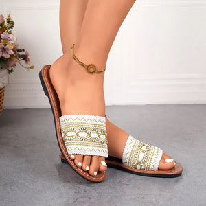 White embroidered artisan open-toe sandals with gold accents and a brown sole.