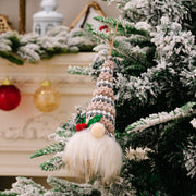 Knitted gnome ornament with striped hat, fluffy white beard, and red berry detail, hanging on a flocked Christmas tree.