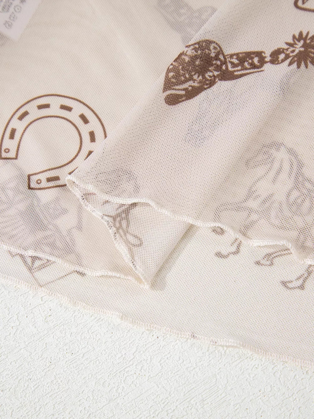Sheer mesh mock neck shirt in cream with brown Western print, featuring horseshoes and spurs.