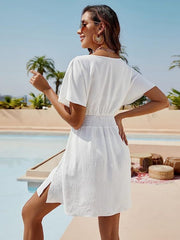 White shirred waistline flutter sleeve mini dress with side slits, styled for the beach.