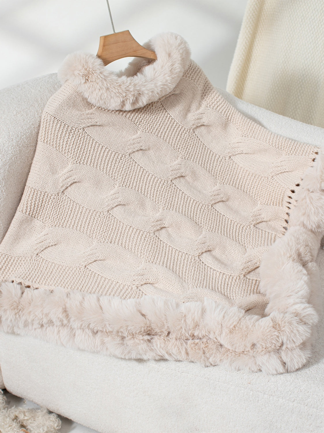 Eggshell cable knit poncho with faux fur trim and cowl neck.