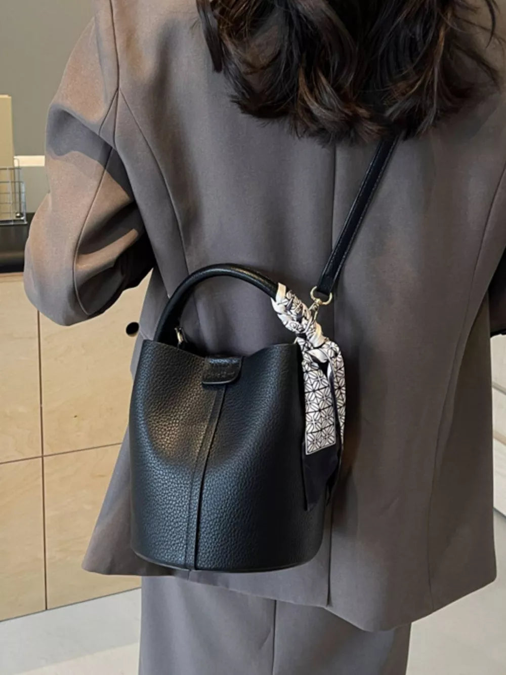 Black pebbled leather bucket bag with decorative scarf detail on strap.