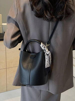 Black pebbled leather bucket bag with decorative scarf detail on strap.