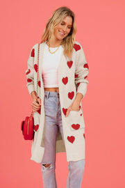 Cream longline knit cardigan with red heart motif, pockets, and open front.