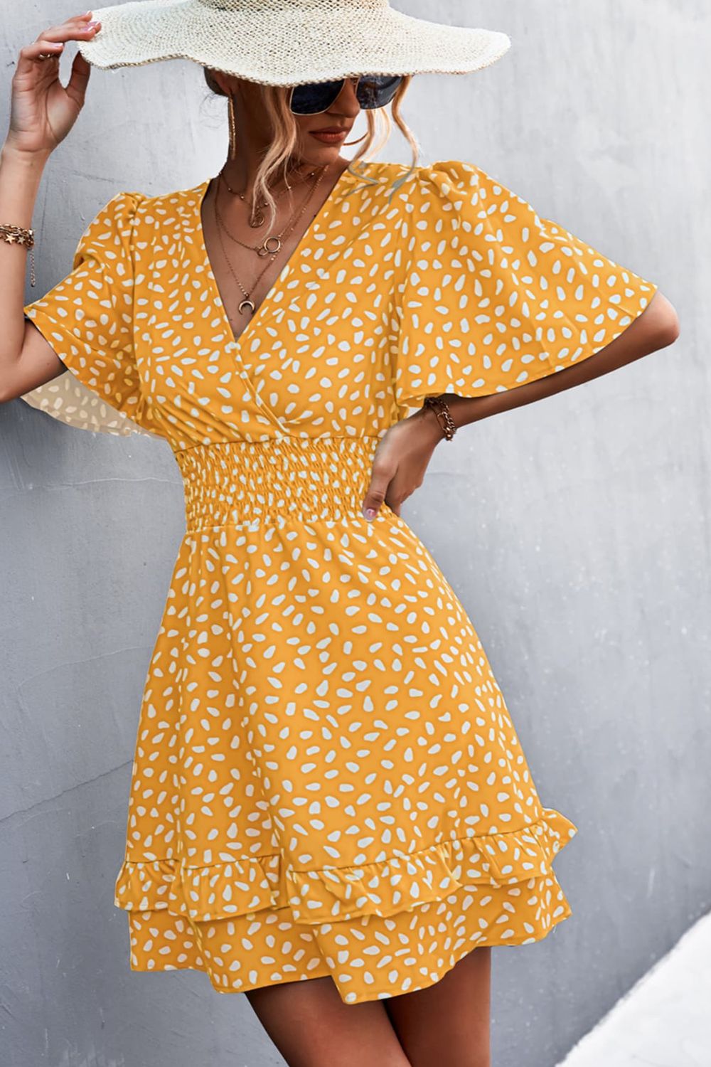 Mustard mini dress with white speckle print, flutter sleeves, V-neck, smocked waist, and ruffled hem.