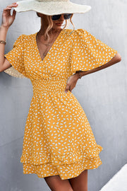 Mustard mini dress with white speckle print, flutter sleeves, V-neck, smocked waist, and ruffled hem.