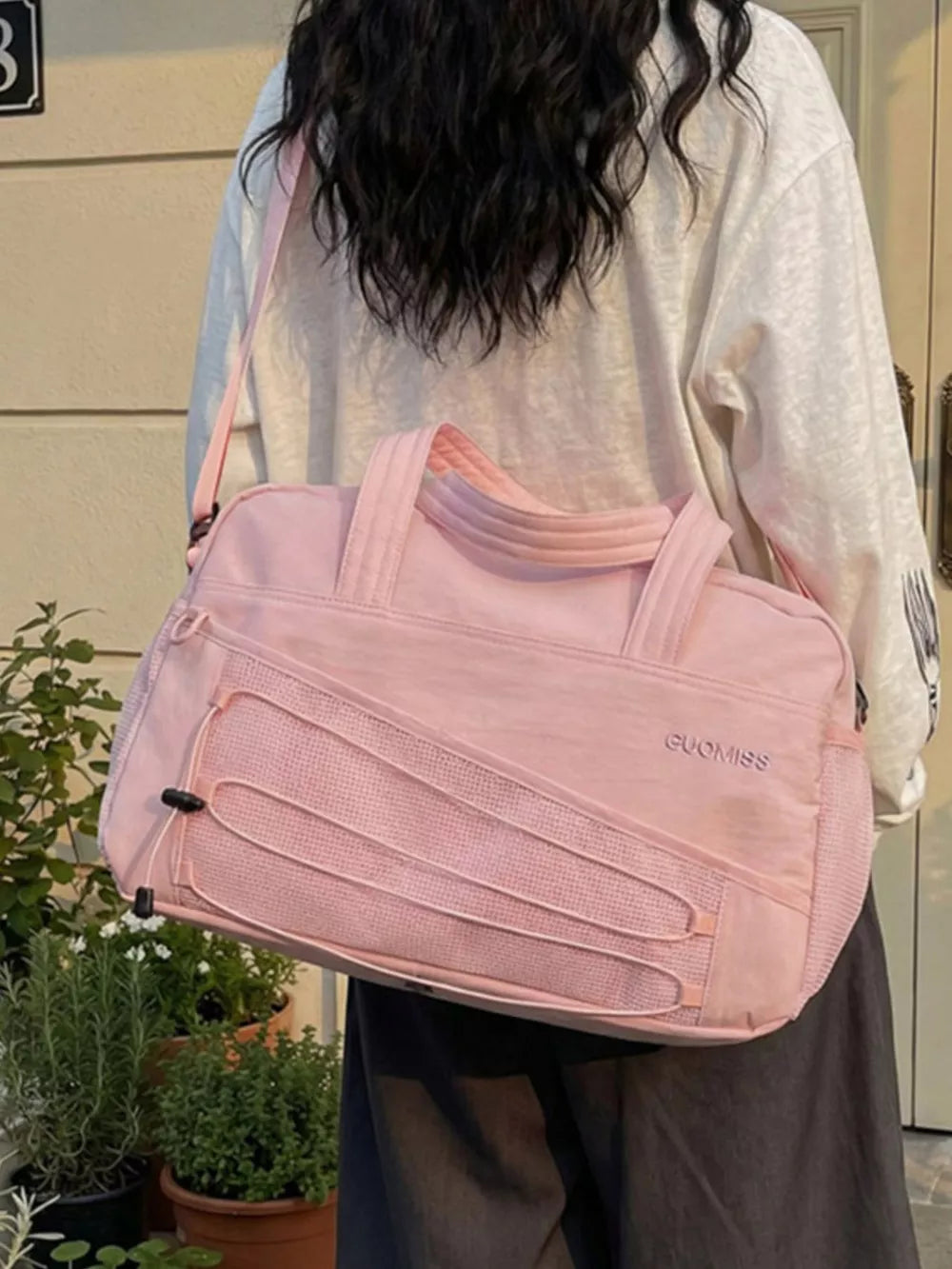 Pink nylon travel organizer bag with bungee cord detail and adjustable strap.