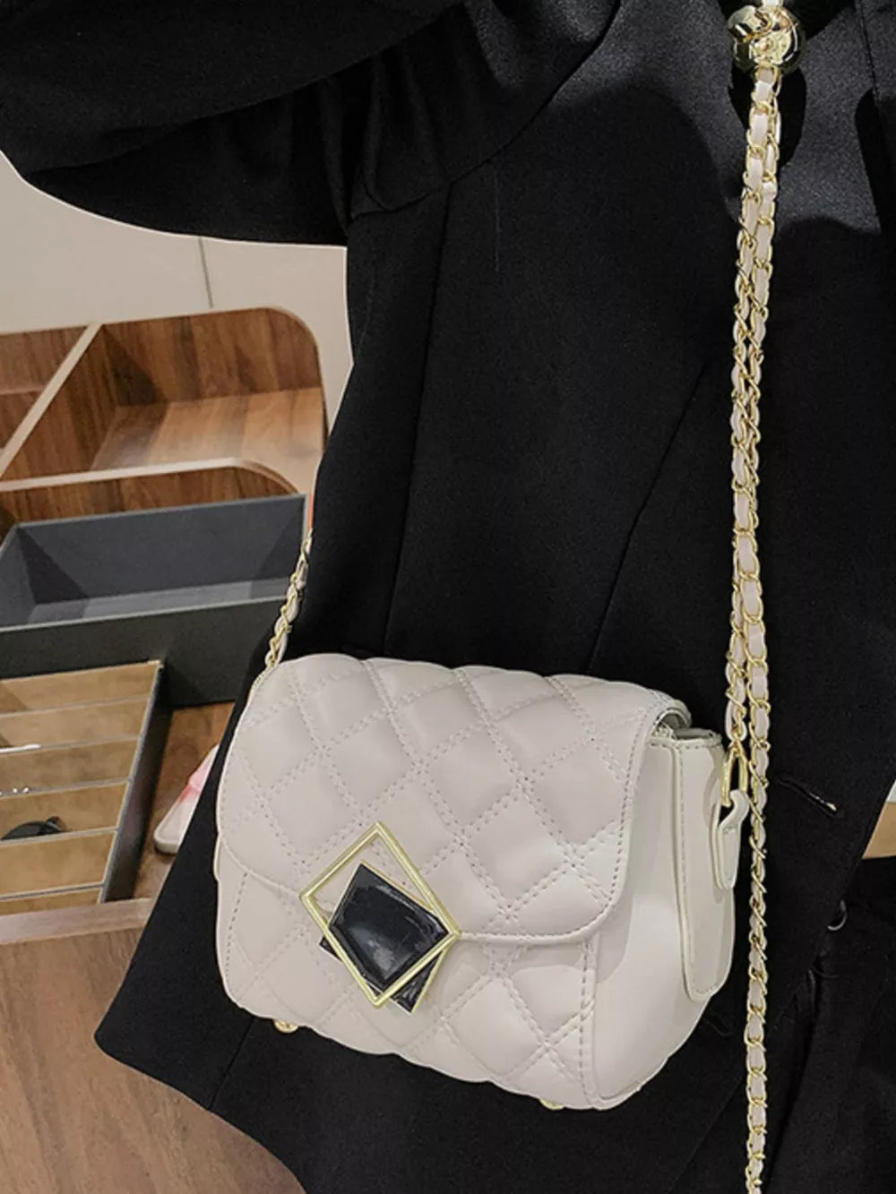 Elegant quilted crossbody bag in white with gold chain strap and geometric charm detail.