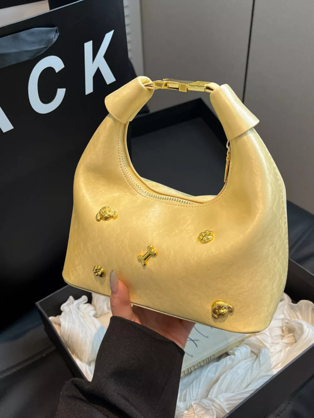 Pastel yellow hobo bag with gold bone and paw print accents and a chain strap detail.