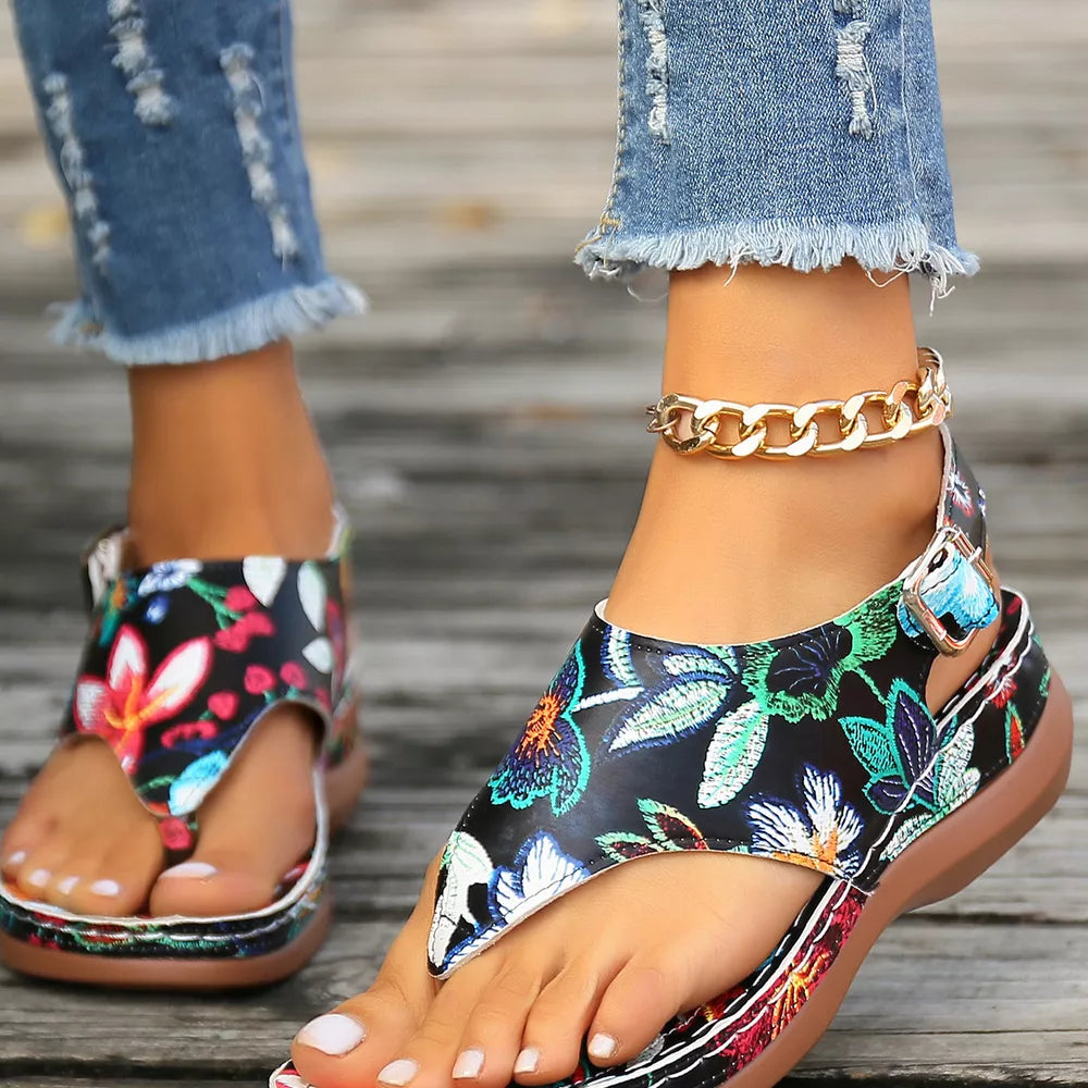 Embroidered floral thong wedge sandals with adjustable ankle strap and gold chain detail.