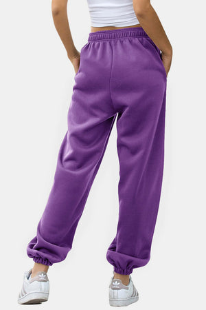 Purple sweatpants with gathered cuffs and pockets, styled with sneakers.