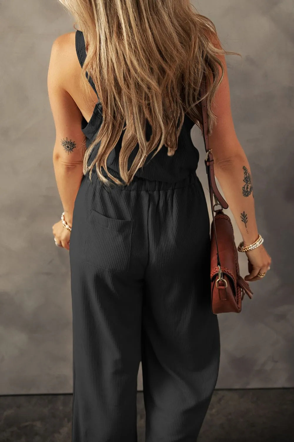 Black waffle knit wide leg jumpsuit with pockets, styled with a brown crossbody bag.