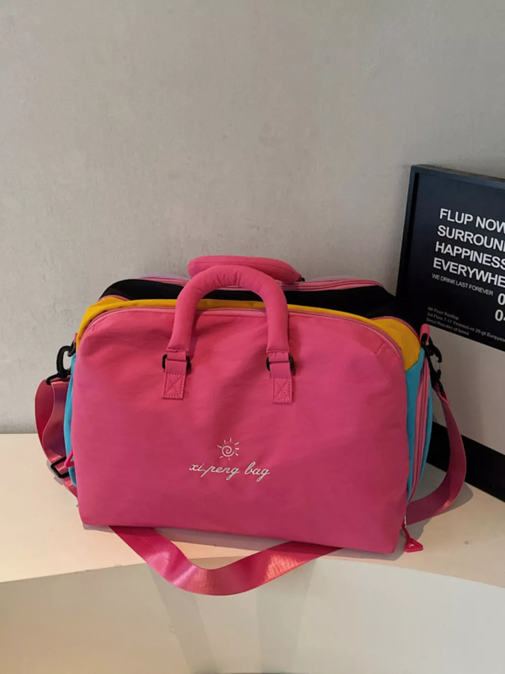Vibrant pink duffel bag with embroidered text and multi-color panels.