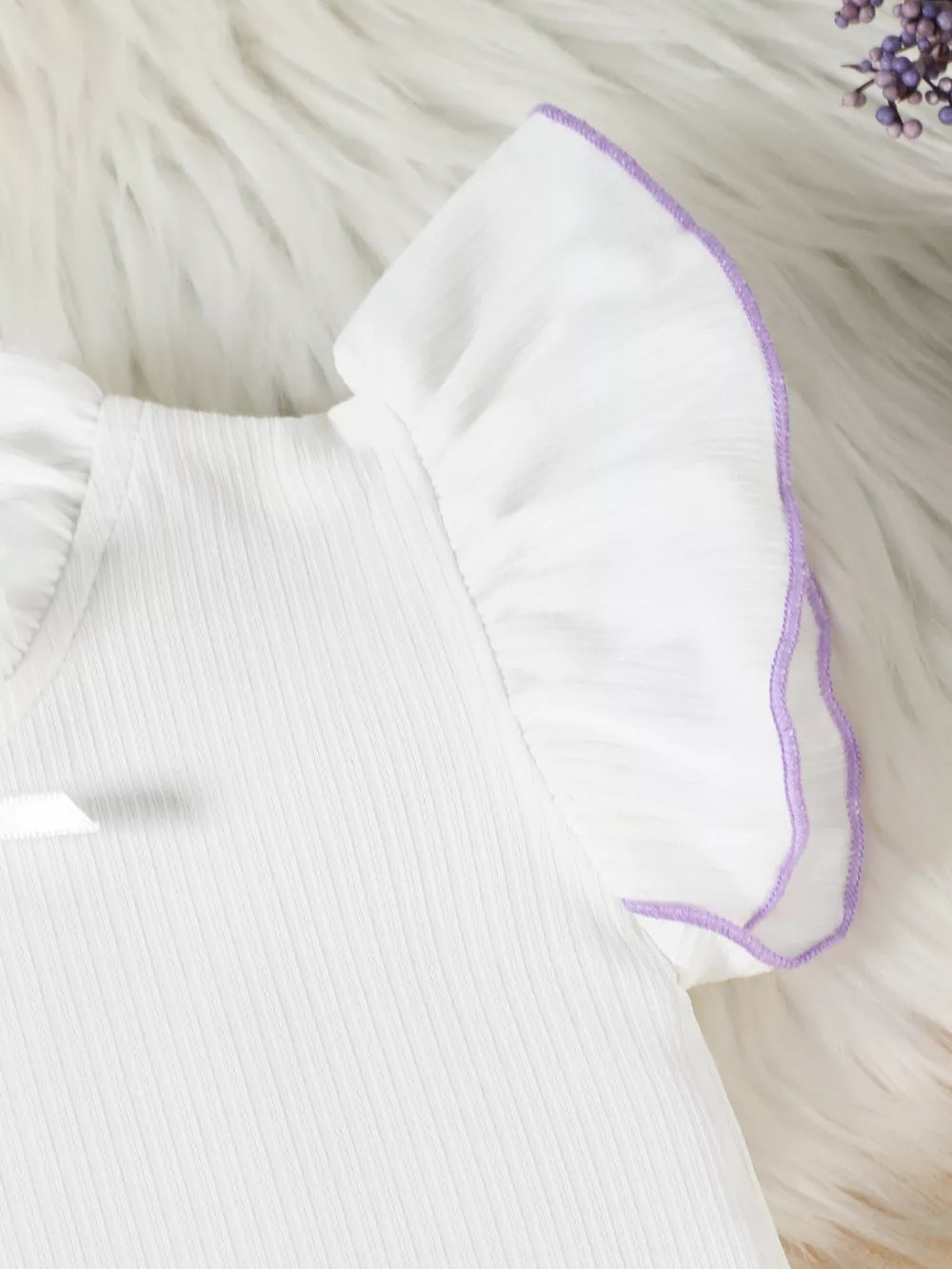 White baby top with purple ruffle trim on sleeves and neckline detail.