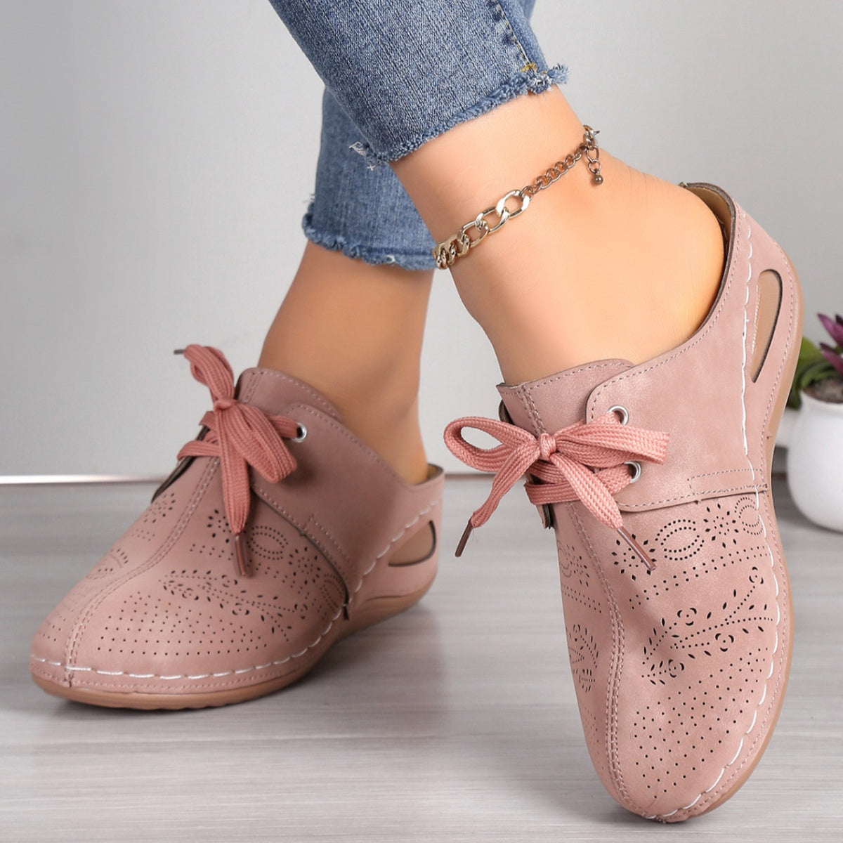 Pink perforated slip-on mules with lace-up detail and cut-out sides.