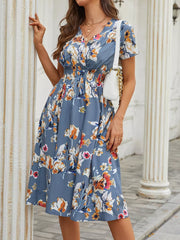 Blue midi dress with vibrant floral pattern, V-neck, short sleeves, and smocked waist.