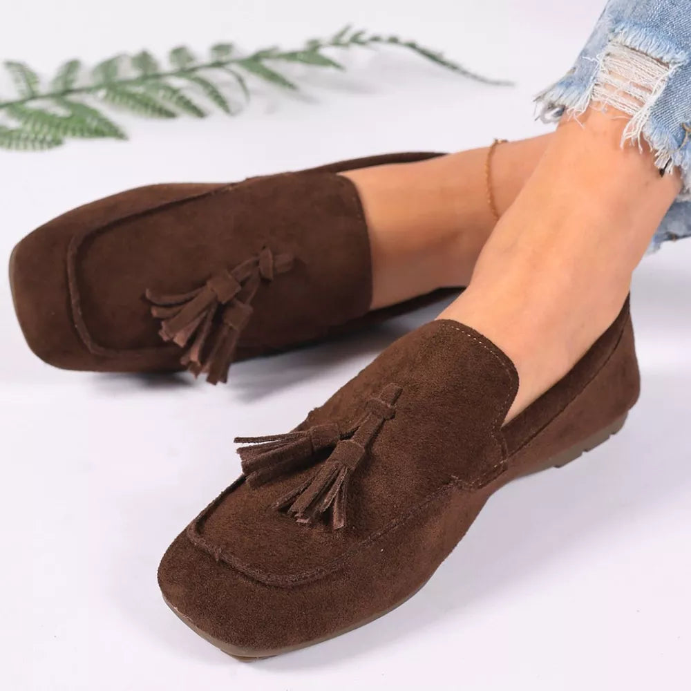 Brown suede slip-on loafers with tassel embellishments.