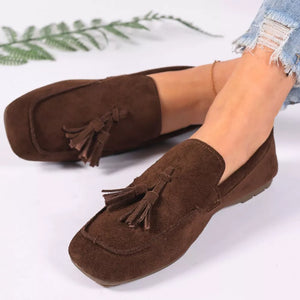 Brown suede slip-on loafers with tassel embellishments.
