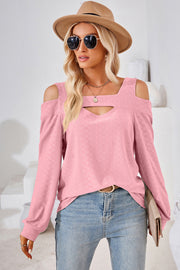 Blush pink long sleeve top with geometric cutout shoulder detail and textured fabric.