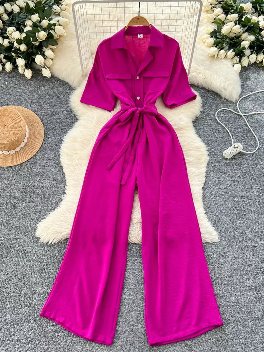 Belted wide-leg jumpsuit in pink with pockets, buttons, and short sleeves.