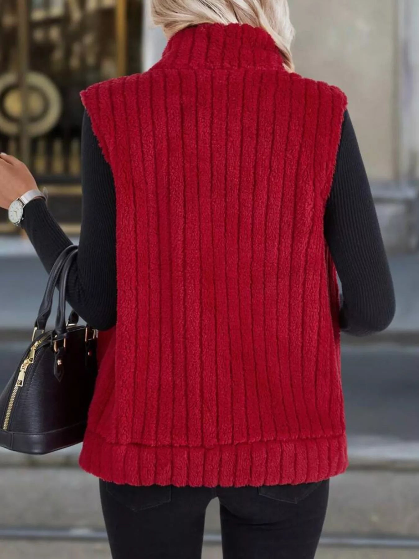 Red fleece zip-up vest with vertical ribbing and mock neck, worn over black sweater.