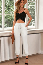 White cropped joggers with pleated waistband and drawstring, cuffed ankles.